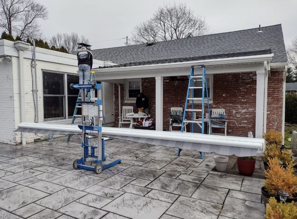 man on blue ladder preparing to install an awning on a house